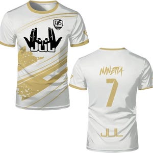 May include: A white short-sleeved t-shirt with gold trim and diagonal gold stripes. The front features a black hand gesture graphic above the text JUL and a small logo. The back displays the name NINETTA, the number 7, and the text JUL in gold.