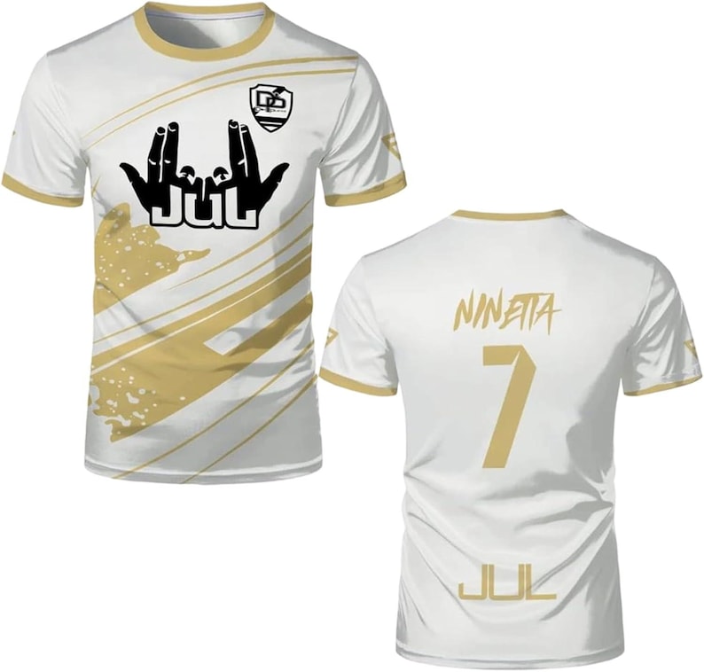 May include: A white short-sleeved t-shirt with gold trim and diagonal gold stripes. The front features a black hand gesture graphic above the text JUL and a small logo. The back displays the name NINETTA, the number 7, and the text JUL in gold.