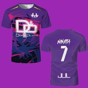May include: A purple short-sleeved t-shirt featuring a front graphic with the text D&P and DOR PLATINE, and a back graphic with the name NINETTA, the number 7, and the text JUL. The design includes abstract dark blue and pink paint splatter patterns.