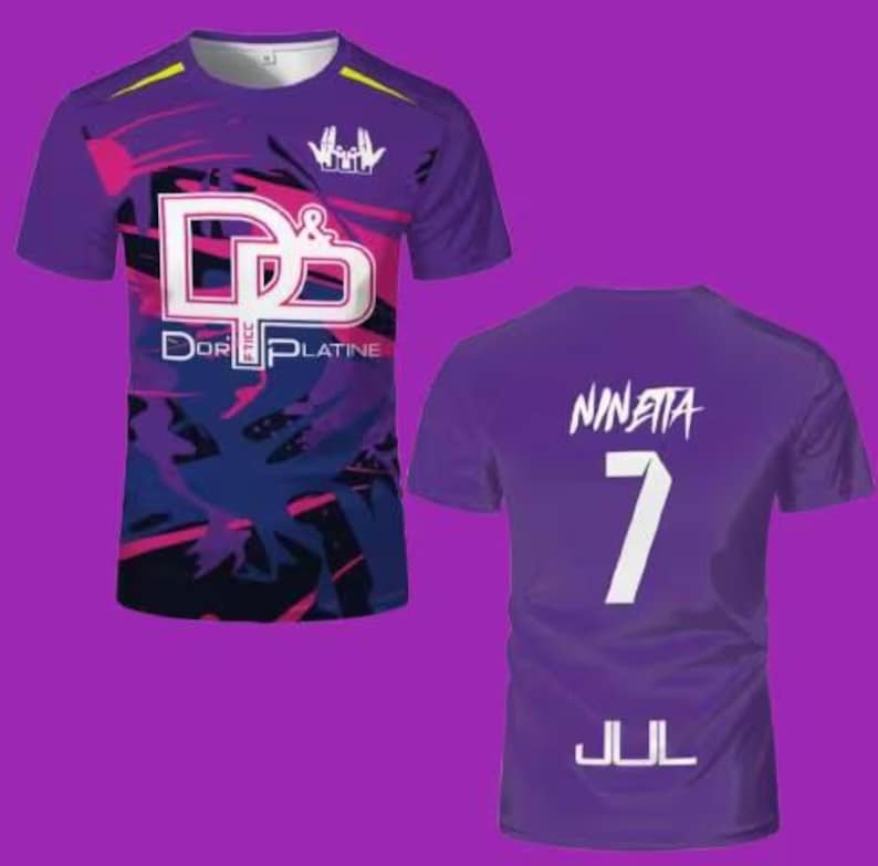May include: A purple short-sleeved t-shirt featuring a front graphic with the text D&P and DOR PLATINE, and a back graphic with the name NINETTA, the number 7, and the text JUL. The design includes abstract dark blue and pink paint splatter patterns.
