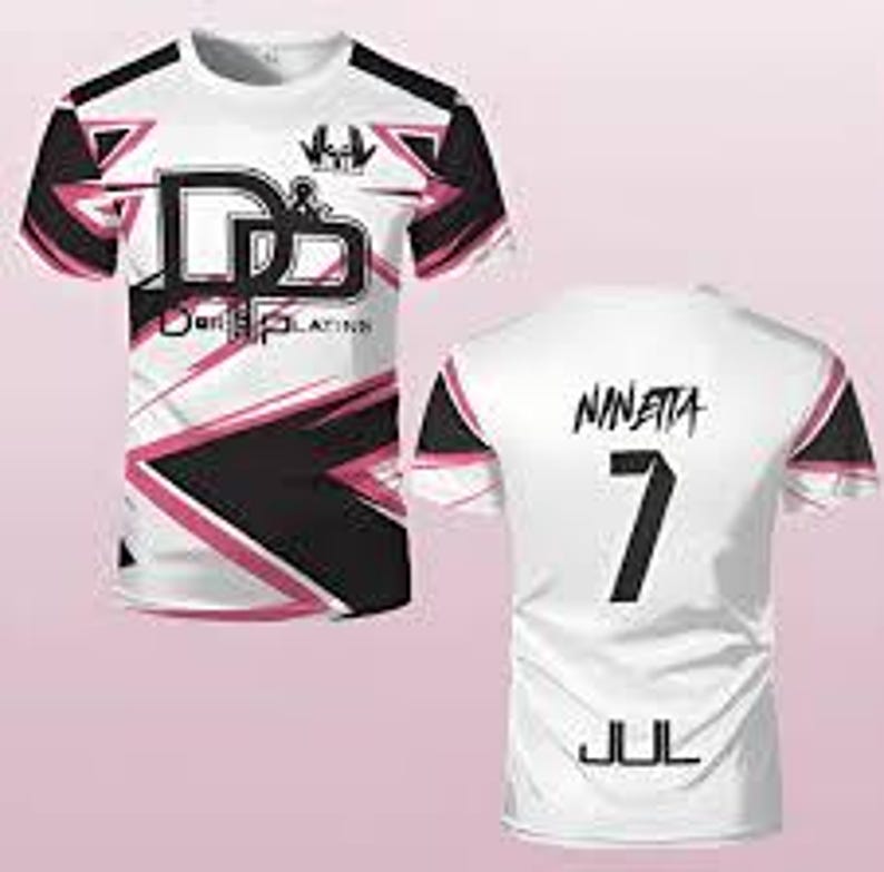 May include: A short-sleeved t-shirt featuring a white base with black and pink geometric patterns. The front displays the text "D&B" and "D&B PLATINS" with a small logo. The back shows the name "NINETTA", the number "7", and the text "JUL".