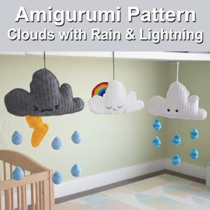 Può includere: Tre decorazioni di nuvole all'uncinetto sono appese al soffitto. Una è grigia con un fulmine giallo e gocce di pioggia blu. Un'altra è bianca con un arcobaleno e la terza è bianca con gocce di pioggia blu. Il testo "Amigurumi Pattern Clouds with Rain & Lightning" è in alto.