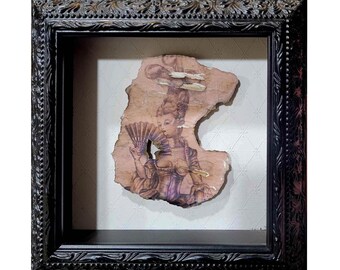 May include: A framed artwork featuring a black and white drawing of a woman in a vintage dress holding a fan. The drawing is on a piece of paper that has been torn and aged, giving it a distressed look. The frame is black with ornate detailing.