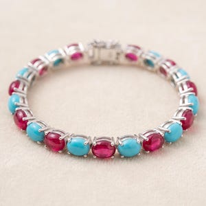 May include: A silver-toned link bracelet featuring alternating oval-shaped cabochon stones in vibrant turquoise blue and deep magenta red. The stones are set in individual metal prongs and connected by a secure metal clasp mechanism at the top.