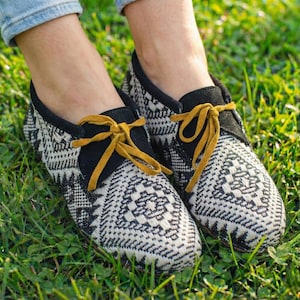 May include: Pair of black and white patterned shoes with yellow laces. The shoes have a geometric design and a black suede collar. The shoes are on a bed of green grass.