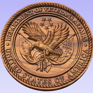 May include: A detailed wooden carving of the United States Department of Veterans Affairs seal. The seal features an eagle with outstretched wings, flags, stars, and the text "UNITED STATES OF AMERICA" and "DEPARTMENT OF VETERANS AFFAIRS". The carving is circular with a rope-like border.