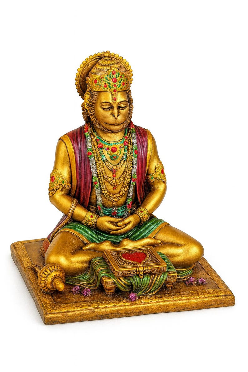 May include: A gold-colored statue of a seated deity with a monkey-like face, adorned with ornate jewelry and a headdress. The figure wears a red and green garment and sits on a gold-colored base, with a small box in front.