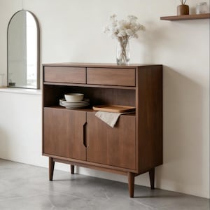 以下が含まれることがあります： 2つの引き出し、オープンシェルフ、2つのドアが付いた下部キャビネットを備えた、ミッドセンチュリーモダンスタイルの木製キャビネット。キャビネットは温かみのある茶色で、先細りの脚が付いています。白い花の入った花瓶が上に置かれています。