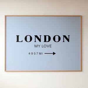May include: A framed wall art piece with a light blue background and the words "LONDON MY LOVE" in black. Below the text is "4957 MI" with an arrow pointing right. The frame is a light brown color.