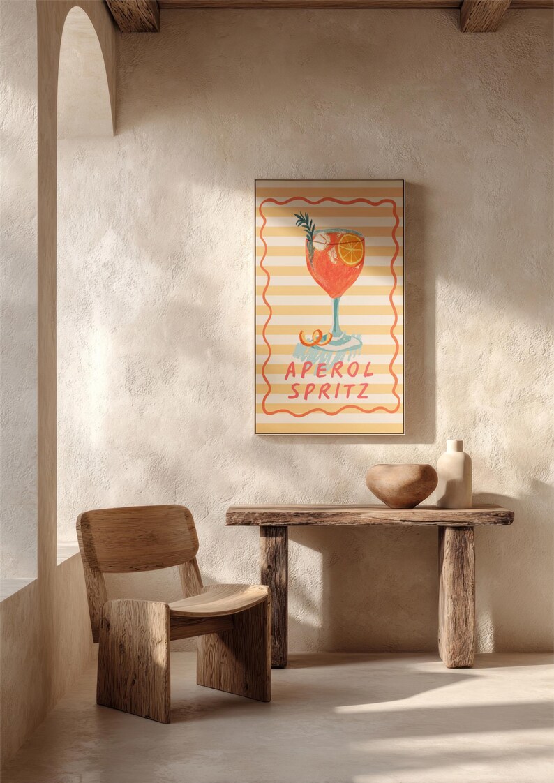K&ouml;nnte beinhalten: Ein gerahmter Druck mit einer Illustration eines Aperol Spritz Cocktails. Das Kunstwerk zeigt einen leuchtend orangefarbenen Cocktail mit Rosmarin und einer Orangenscheibe auf gestreiftem Hintergrund. Die Worte "APEROL SPRITZ" sind darunter geschrieben.