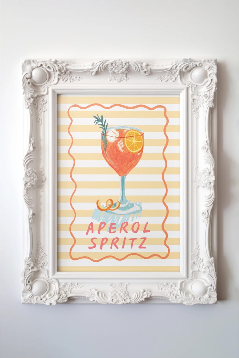 K&ouml;nnte beinhalten: Ein gerahmter Druck mit einer Illustration eines Aperol Spritz Cocktails. Das Kunstwerk zeigt einen leuchtend orangefarbenen Cocktail mit einer Orangenscheibe und einem Rosmarinzweig, vor einem gelb-wei&szlig; gestreiften Hintergrund. Die Worte "APEROL SPRITZ" sind in Rosa geschrieben.