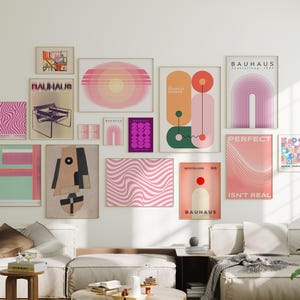 May include: A collection of framed art prints in various sizes and designs, including abstract geometric shapes, wavy patterns, and Bauhaus-style posters. The color palette includes pinks, oranges, greens, and purples. The prints are displayed on a white wall above a sofa.