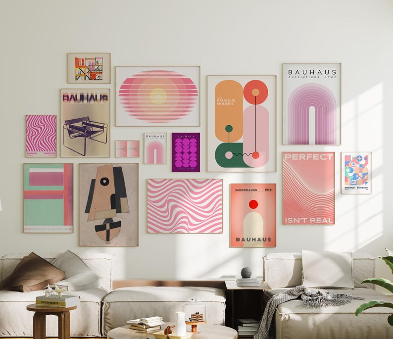 May include: A collection of framed art prints in various sizes and designs, including abstract geometric shapes, wavy patterns, and Bauhaus-style posters. The color palette includes pinks, oranges, greens, and purples. The prints are displayed on a white wall above a sofa.
