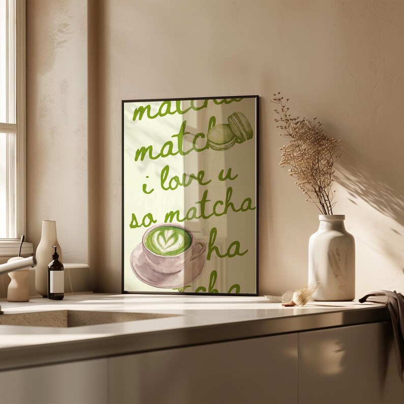 May include: A framed print with the words "matcha, i love u so matcha" in green script. The print features a matcha latte with latte art and a macaron. The print is displayed on a kitchen counter.