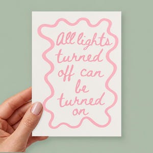 May include: A rectangular white card featuring a pink wavy border and the handwritten pink text All lights turned off can be turned on. The design is centered on the card, which has a clean, simple layout with a soft color palette.