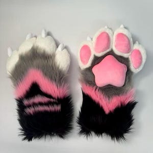 May include: A pair of furry paw gloves in a playful design. The gloves feature a color scheme of black, gray, and pink, with white claws and pink paw pads. The plush material gives a soft, tactile appearance, perfect for cosplay or costume use.