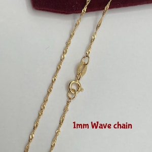 May include: A gold-colored 1mm wave chain necklace. The chain has a delicate, twisted design and a spring ring clasp. The text "1mm Wave chain" is visible in the image.