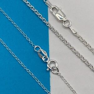 May include: A silver chain necklace featuring a polished finish and a secure lobster claw clasp. The metal links are uniform and rounded, creating a classic cable chain design. The clasp is stamped with 925 and Italy, indicating sterling silver.