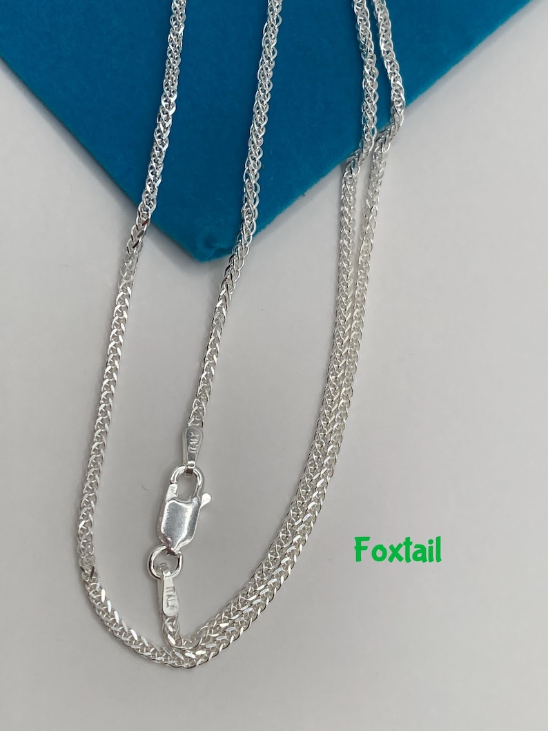 May include: A silver foxtail chain necklace with a lobster clasp. The necklace is displayed on a blue surface with the word "Foxtail" in green text.