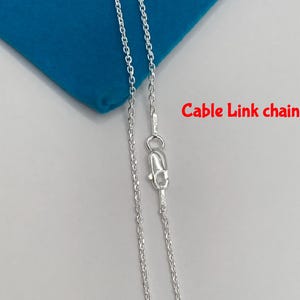 May include: A silver cable link chain necklace with a lobster clasp. The chain is displayed on a blue surface. The text "Cable Link chain" is in red.