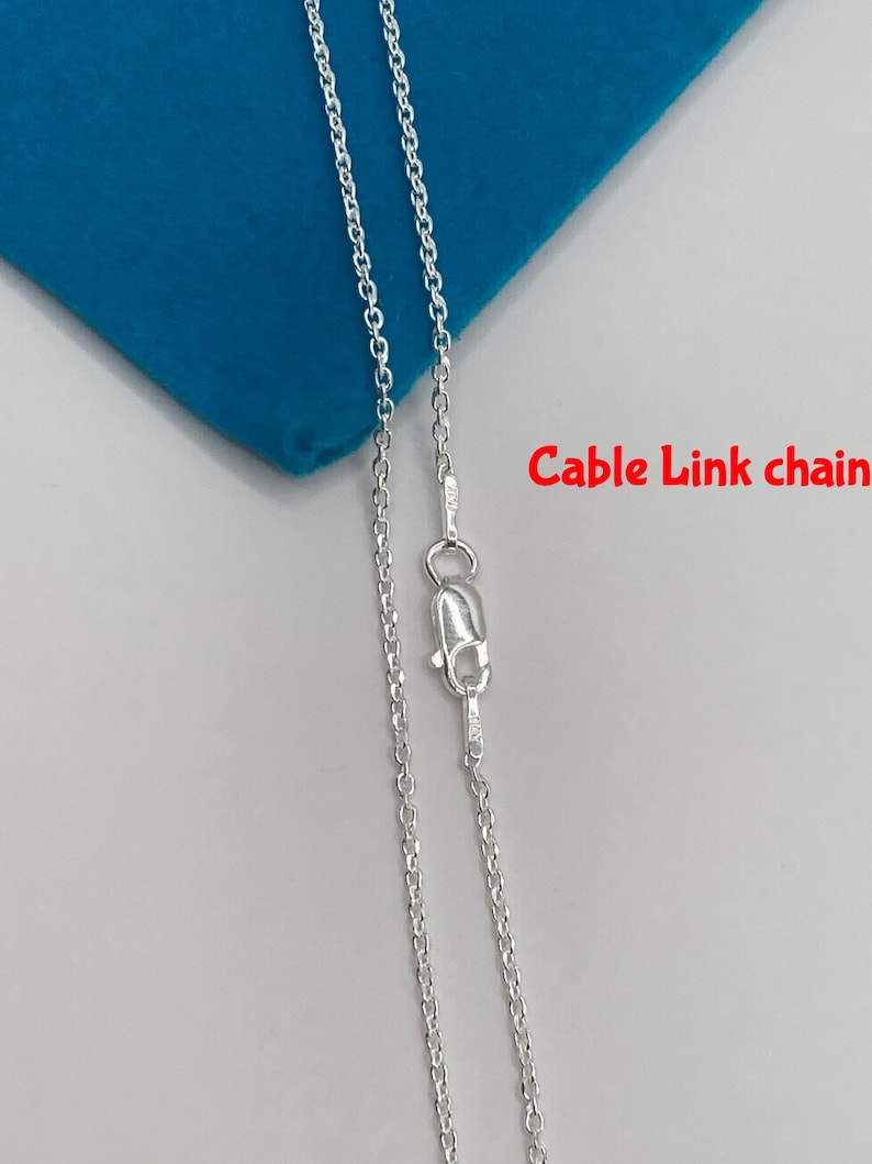 May include: A silver cable link chain necklace with a lobster clasp. The chain is displayed on a blue surface. The text "Cable Link chain" is in red.