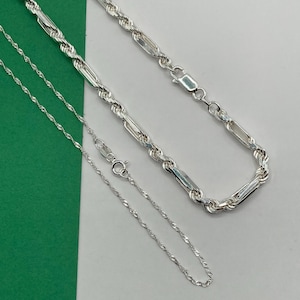 May include: Two silver-toned metal chains. The thicker chain features a combination of twisted rope links and elongated smooth rectangular bars. The thinner chain is a delicate, spiraled singapure style chain. Both chains have lobster clasps.