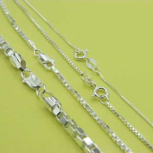 May include: A collection of four silver-toned box chains of varying thicknesses, each featuring a polished metallic finish and a secure lobster claw clasp. The chains are arranged diagonally, showcasing the square-linked design of each individual chain.