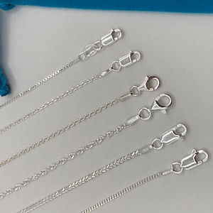May include: A collection of silver-colored chain necklaces with various link styles, including rope, curb, and box chains. Each chain is secured with a lobster clasp. The chains are displayed against a light background.