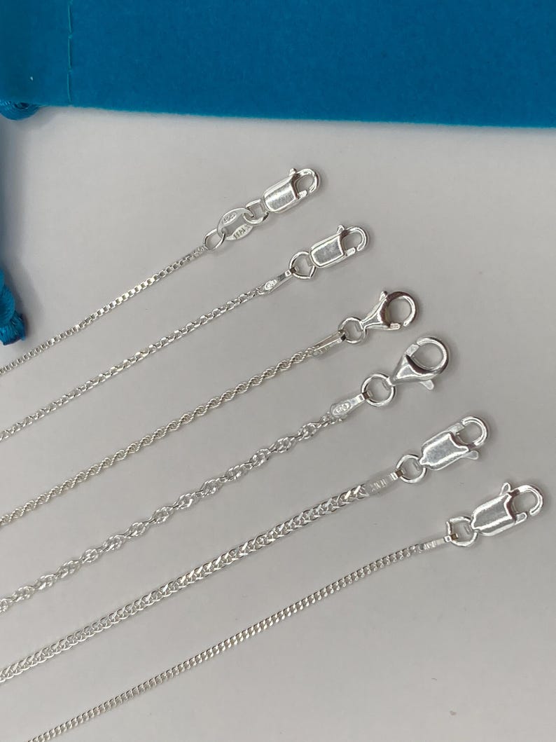 May include: A collection of silver-colored chain necklaces with various link styles, including rope, curb, and box chains. Each chain is secured with a lobster clasp. The chains are displayed against a light background.