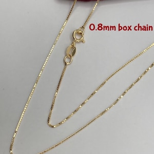 May include: A delicate gold-colored necklace with a box chain design. The chain is 0.8mm thick and features a lobster clasp closure. The necklace is displayed against a neutral background, highlighting its fine details.