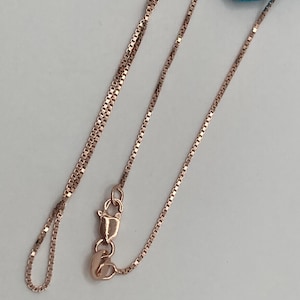May include: Rose gold necklace featuring a delicate box chain design. The chain is finely crafted with small, square links and a lobster clasp closure. The necklace is displayed on a light background.
