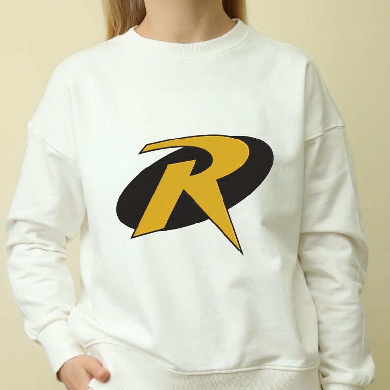 May include: White sweatshirt featuring a large yellow "R" logo with a black oval background. The logo is centered on the front of the long-sleeved, crew neck top. The sweatshirt is made of a soft material.