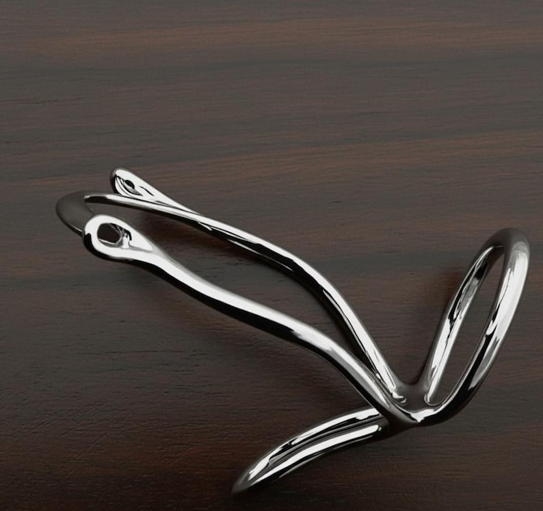 Puede incluir: Una escultura de metal plateado pulido con un dise&ntilde;o abstracto y fluido. La pieza presenta l&iacute;neas curvas y bucles, creando una sensaci&oacute;n de movimiento. La escultura est&aacute; sobre un fondo de madera oscura.