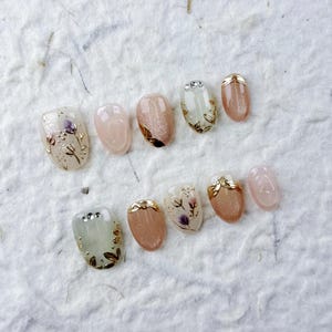 Korte ovale druk op de nagels in zachtroze en beige. Gouden bladeren, paarse bloemen, subtiele glans, perfect voor dagelijks woon-werkverkeer en elegante dates