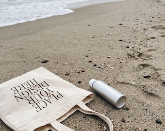 Leere Canvas-Einkaufstasche und weiße Flasche auf Sandy Beach PSD