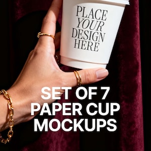 以下が含まれることがあります： 「PLACE YOUR DESIGN HERE」の文字が入った白い紙コップのモックアップを、金色の指輪とブレスレットをつけた手で持っています。画像には「SET OF 7 PAPER CUP MOCKUPS」の文字も表示されています。背景は濃いバーガンディ色です。