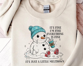Può includere: Felpa color crema con un pupazzo di neve dei cartoni animati con cappello blu e scarpe rosse, che si scioglie e tiene in mano una bevanda. Il testo recita: "It's fine, I'm fine, everything is fine. It's just a little meltdown."