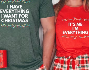 May include: Matching Christmas pyjamas set. One person wears a green t-shirt with the text "I HAVE EVERYTHING I WANT FOR CHRISTMAS" and holds a red mug. The other wears a red t-shirt with the text "IT'S ME I'M EVERYTHING" and holds a white mug.
