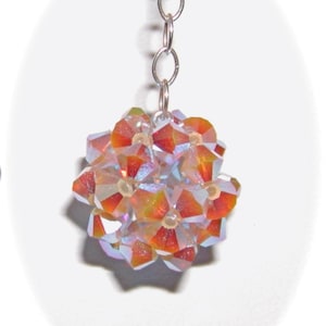 Puede incluir: Una cadena de plata con un racimo de cuentas de cristal iridiscente en tonos naranja y rosa.