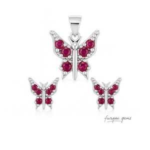 May include: A jewelry set featuring a butterfly pendant and matching earrings. The butterfly designs are crafted in silver and adorned with vibrant red gemstones. The set includes a pendant and two earrings, all with a delicate, detailed design.
