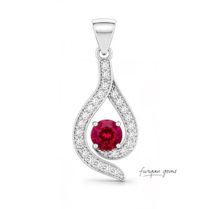 May include: A silver pendant with a teardrop design. The pendant features a vibrant red gemstone at the centre, encircled by a swirling pattern of small, sparkling white gemstones. The brand name "furgan gems" is written in cursive.