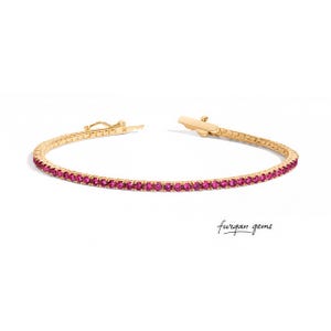 Op de afbeelding: Een gouden tennisarmband met een rij felroze edelstenen. De armband is open, met de sluiting en de delicate zetting van de stenen. De tekst "furgan gems" is in cursief geschreven.