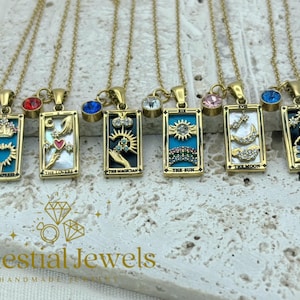 May include: Gold-coloured necklaces with rectangular pendants depicting tarot card designs. Each pendant features a different design, including The Empress, The Lovers, The Magician, The Sun, The Moon, and The Star. Each necklace has a coloured gemstone charm.