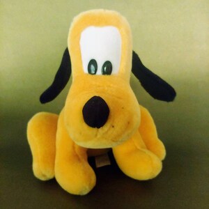 May include: A yellow plush toy dog with black ears and a black nose. The dog has large white eyes with black pupils.