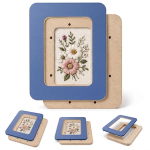 May include: A rectangular wooden embroidery hoop frame consisting of a light-colored wooden base and a blue-painted wooden top piece. The frame holds a piece of off-white fabric featuring an embroidered floral design with white, pink, and green thread.