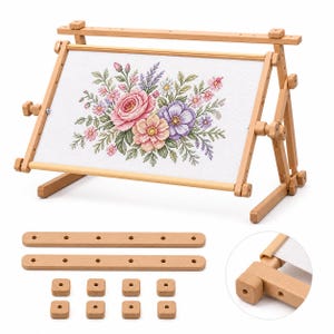 May include: A light-colored wooden embroidery frame stand holding a white fabric panel with a cross-stitched floral bouquet featuring pink, purple, and green threads. Includes two additional wooden bars and eight small square wooden knobs.