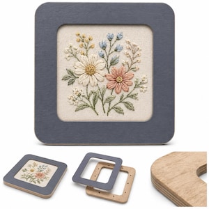 Puede incluir: Una obra de arte cuadrada enmarcada con un diseño floral bordado. El marco es de un gris azulado apagado, y el bordado muestra un ramo de flores en tonos blancos, melocotón, amarillos y azules. Marcos adicionales son visibles.