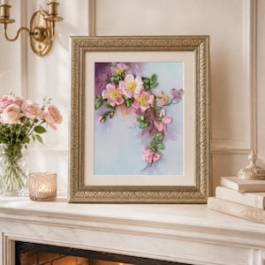 May include: A framed artwork featuring three-dimensional ribbon embroidery of pink flowers with yellow centers and green leaves on a soft, blended pastel background. The piece is encased in an ornate, metallic gold-toned rectangular frame.