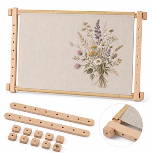 May include: A rectangular wooden embroidery frame holding a piece of beige fabric with a floral bouquet embroidery design. The set includes two additional wooden bars with holes and ten small wooden square knobs for assembly and tension adjustment.