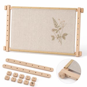 Puede incluir: Un bastidor de bordado rectangular de madera que sostiene una tela de color beige claro con un delicado diseño botánico verde. El conjunto incluye dos barras laterales de madera con orificios y diez pequeños pomos cuadrados de madera.